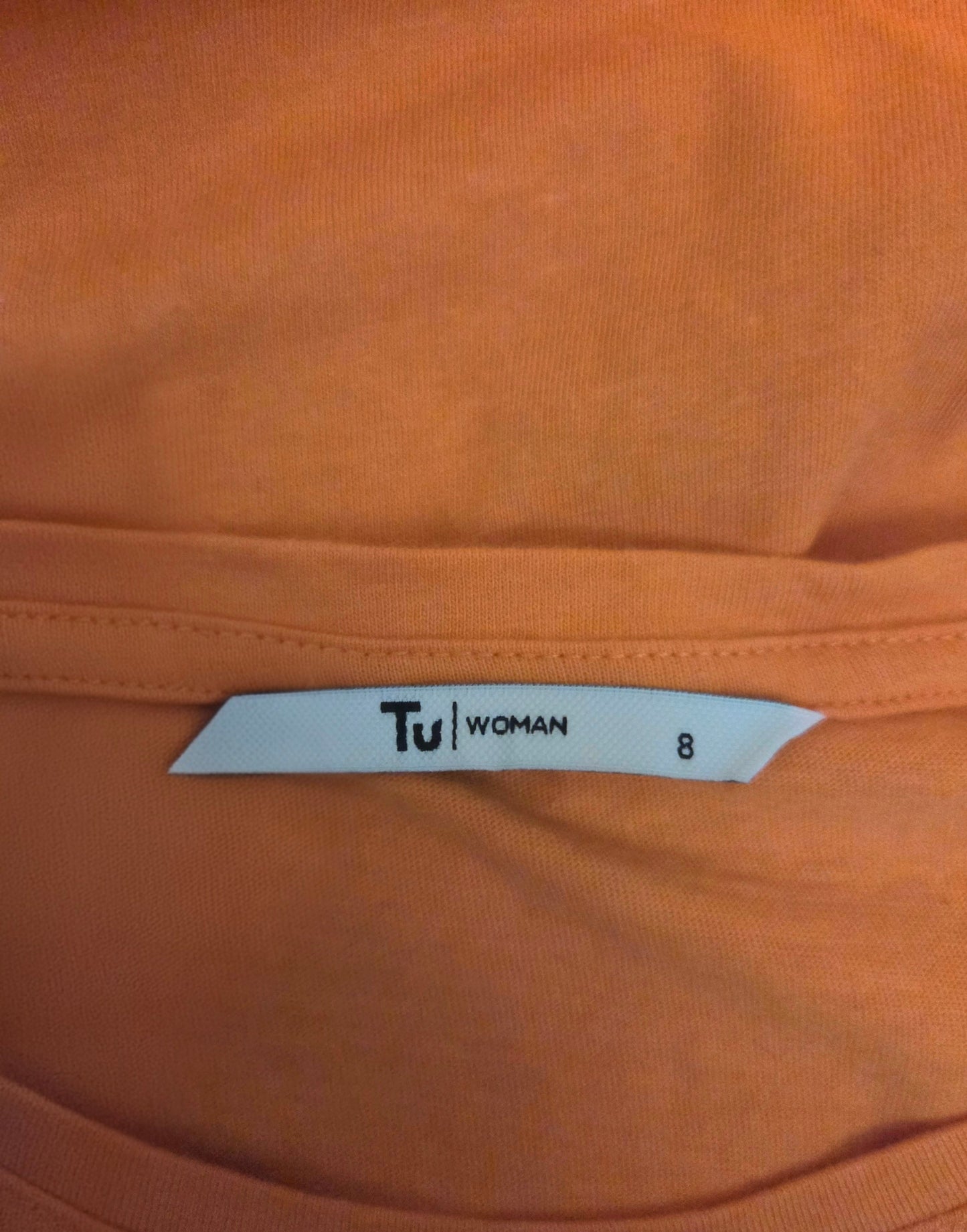Close-up of an orange t-shirt with a 'Tu Woman' size label