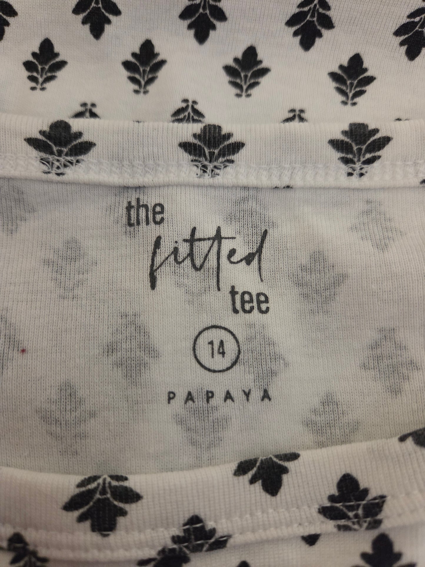 Close-up of fabric with black leaf pattern and 'the fitted tee' branding.
