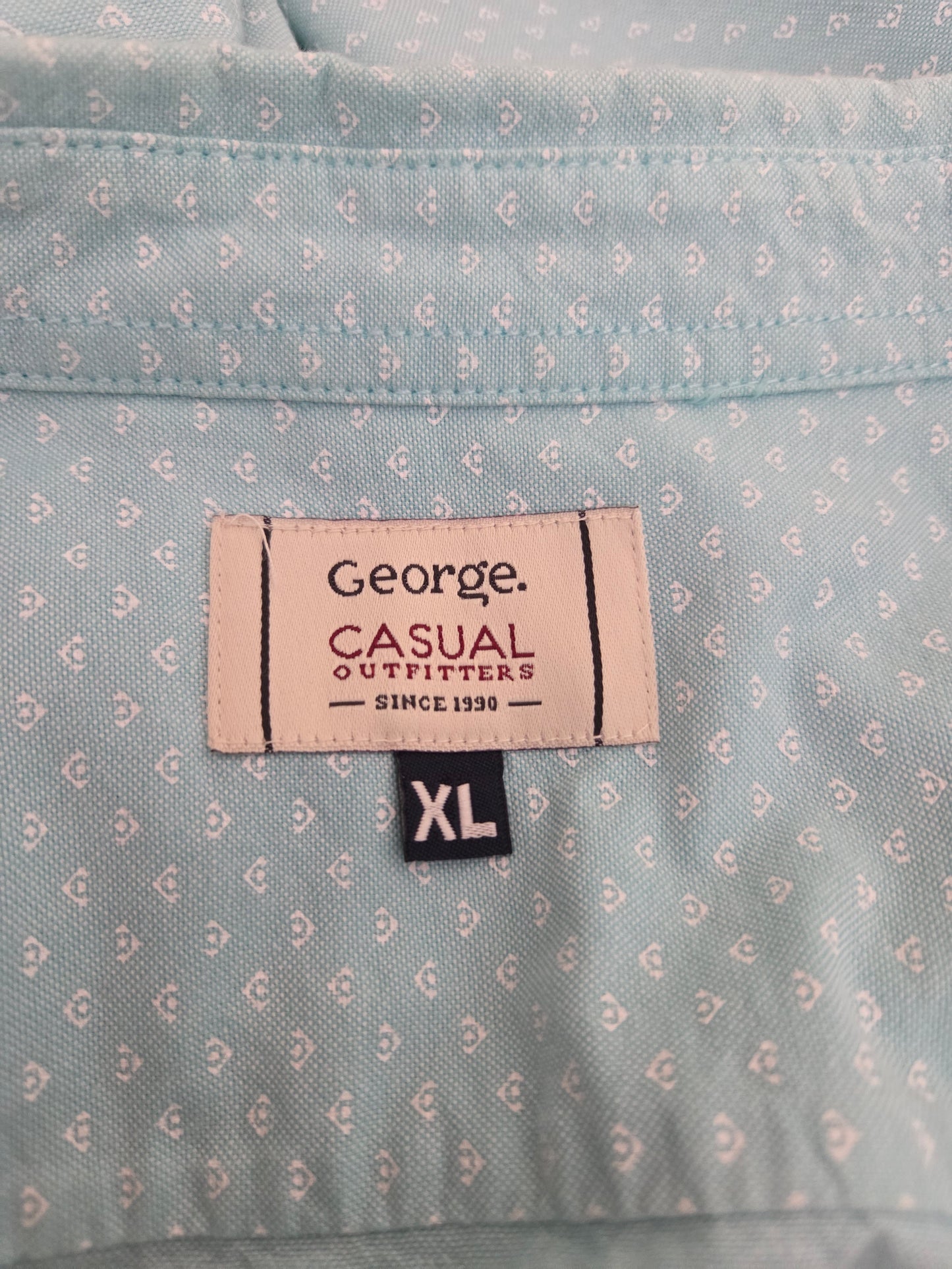 Close-up of a shirt label on a mint green patterned shirt with 'George Casual Outfitters' branding.