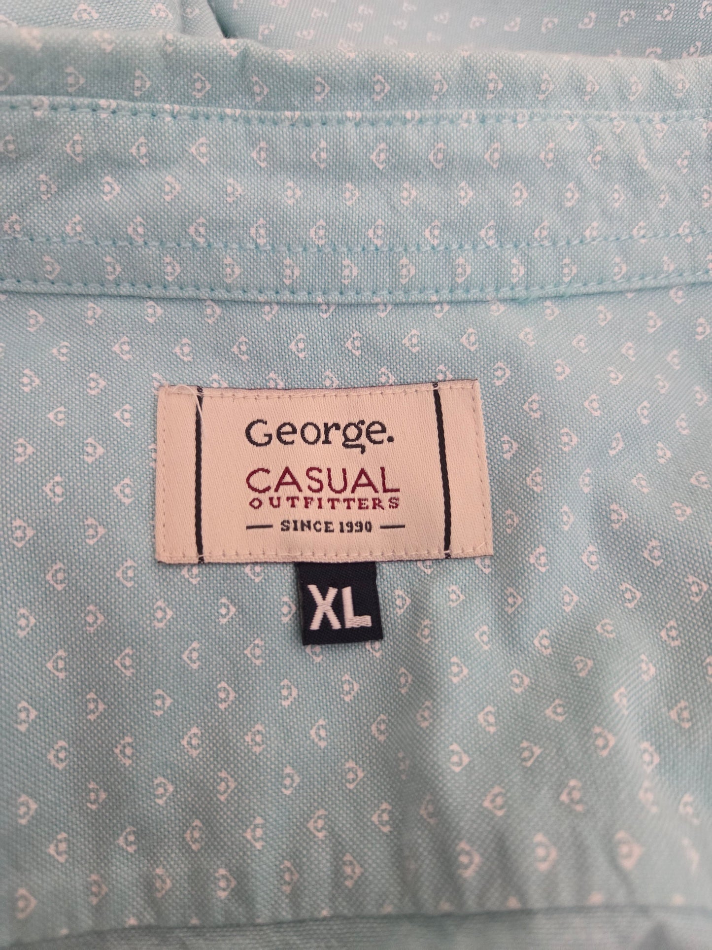 Close-up of a shirt label on a light blue patterned shirt with 'George Casual Outfitters' branding.