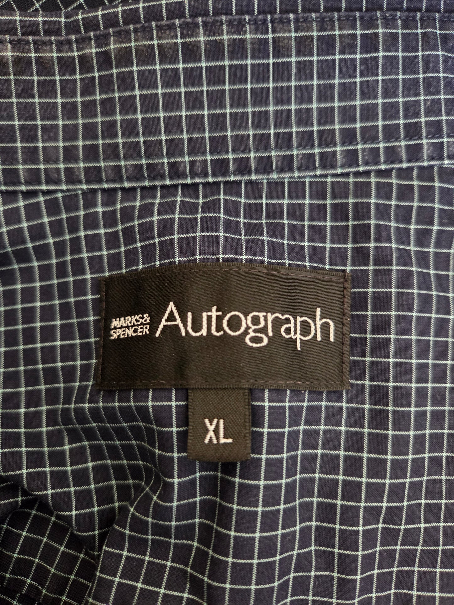 Close-up of a checkered shirt with an Autograph size label on a dark background