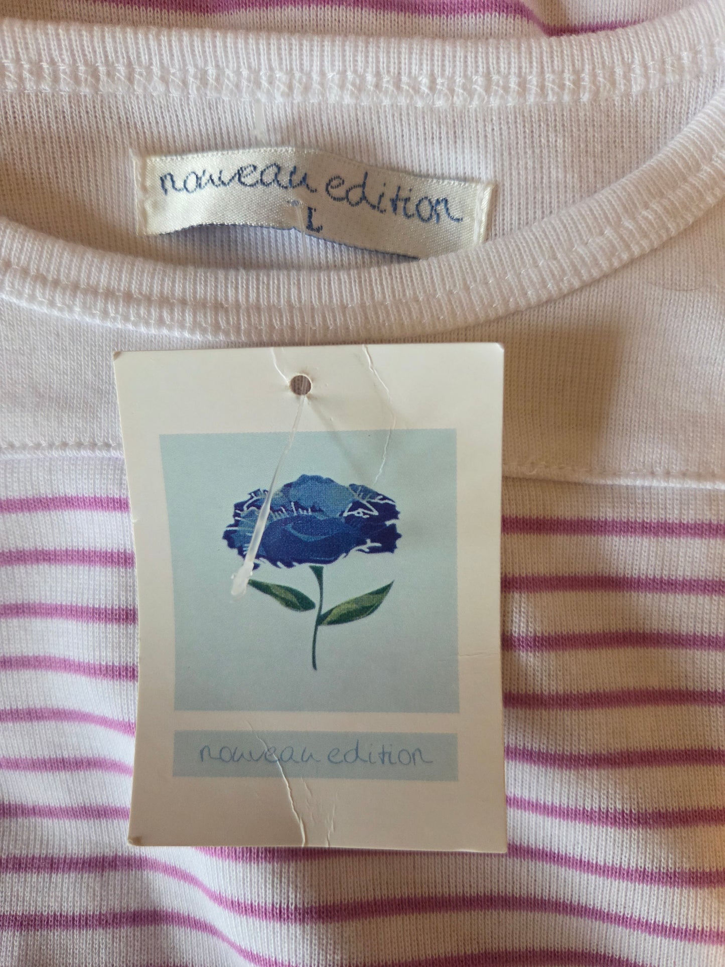 Close-up of a striped shirt with a blue rose tag and 'nouveau edition' label.