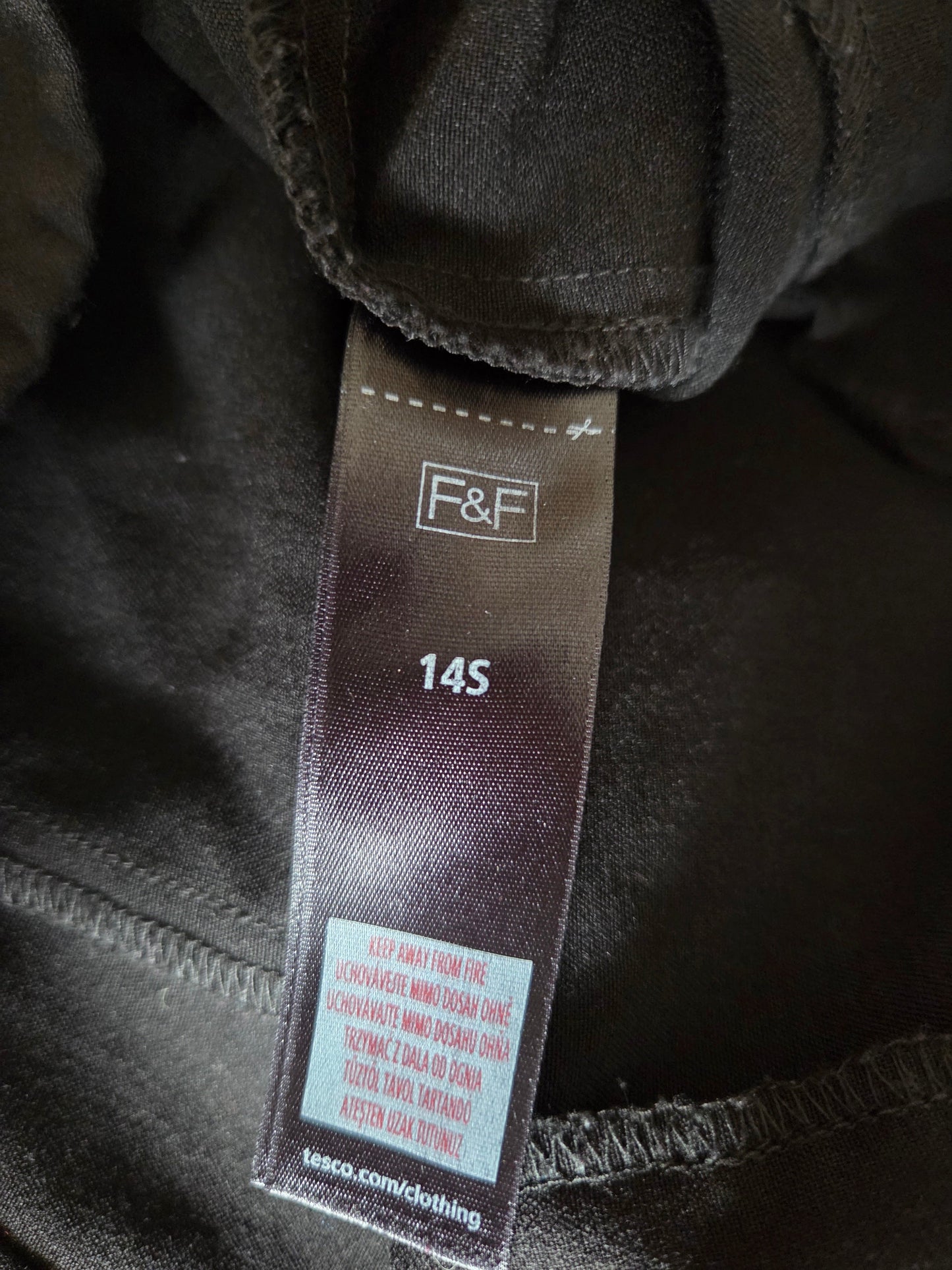 Clothing tag with 'F&F' brand on a dark fabric background