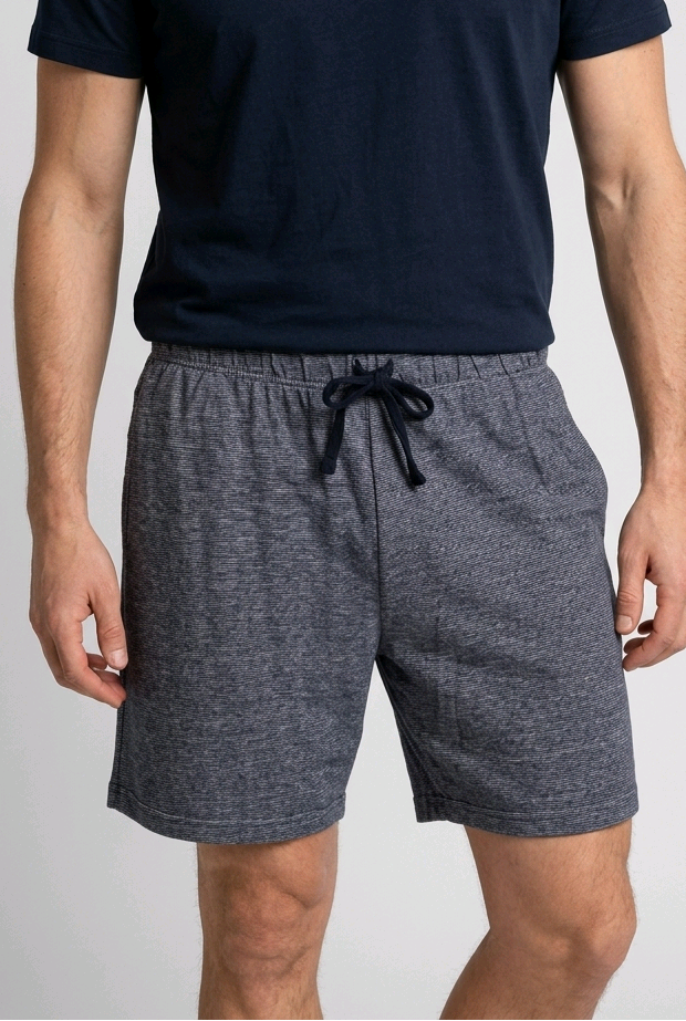 Man wearing a navy t-shirt and gray shorts on a white background