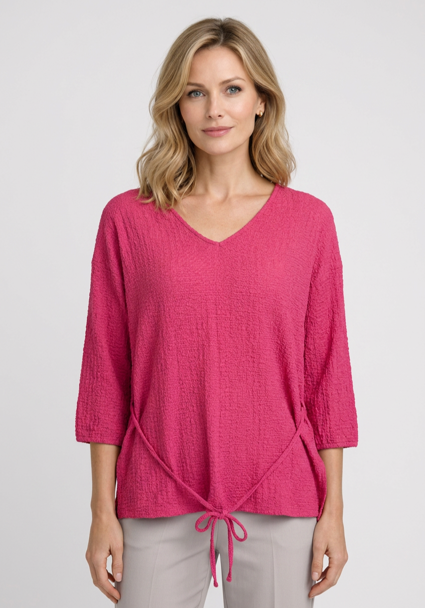 Woman wearing a pink textured top with a tie detail 