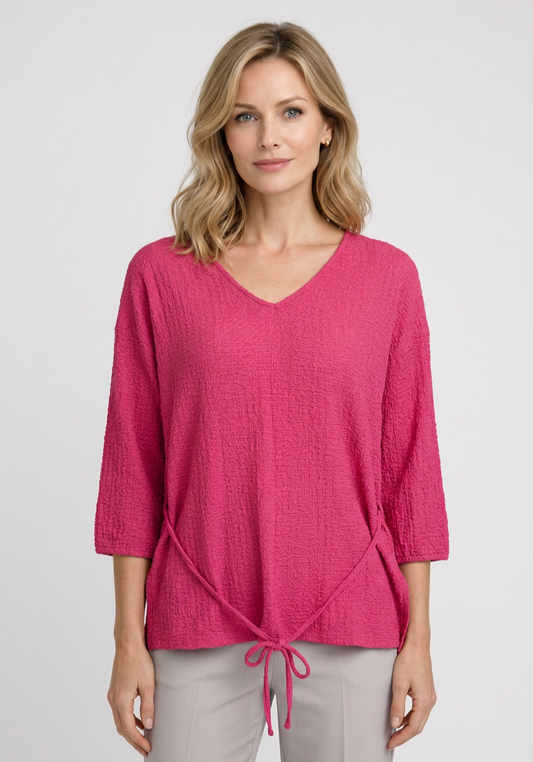 Woman wearing a pink textured top with a tie detail 