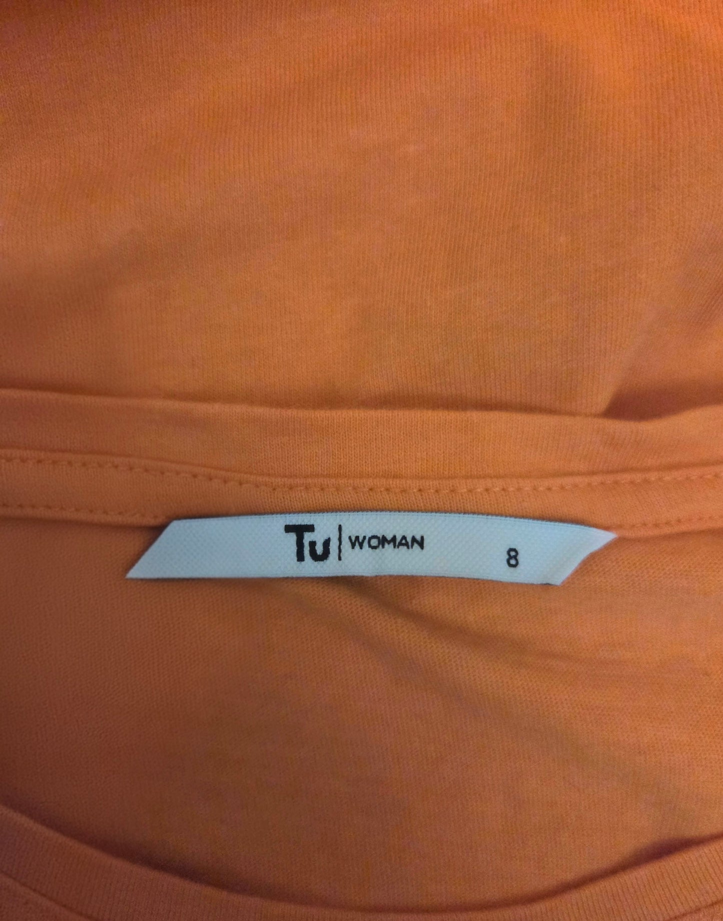 Close-up of an orange t-shirt with a 'Tu Woman' size label 