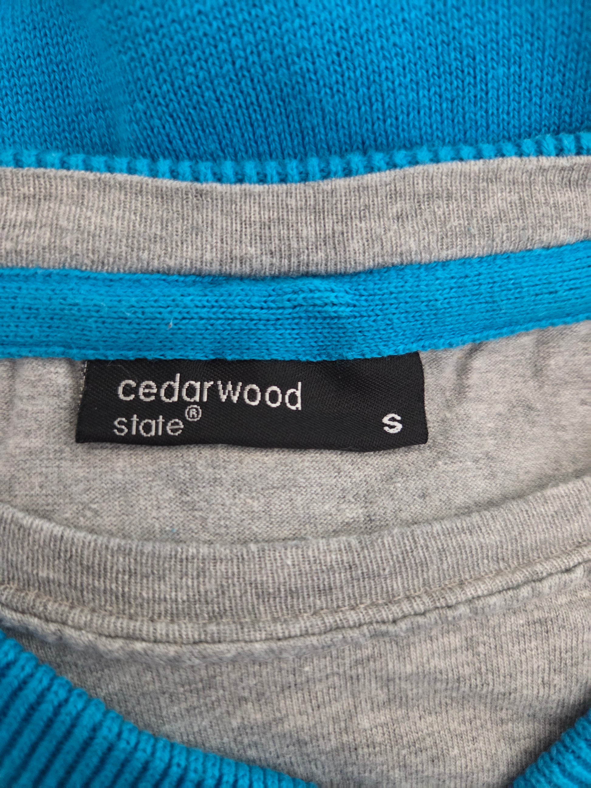 Close-up of a gray sweater with blue trim and a Cedarwood State label.