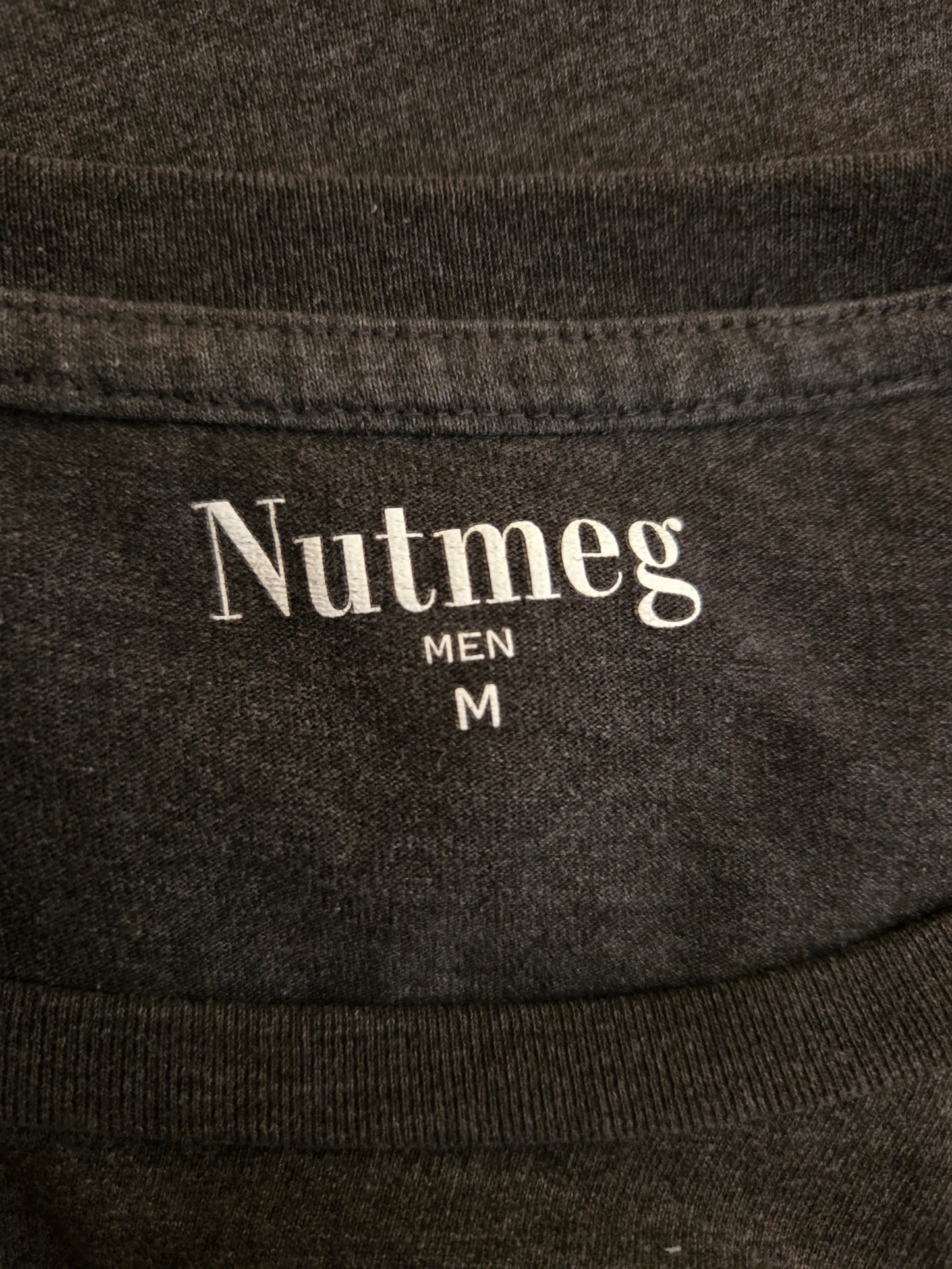 Close-up of a dark fabric with 'Nutmeg Men' branding and size label.