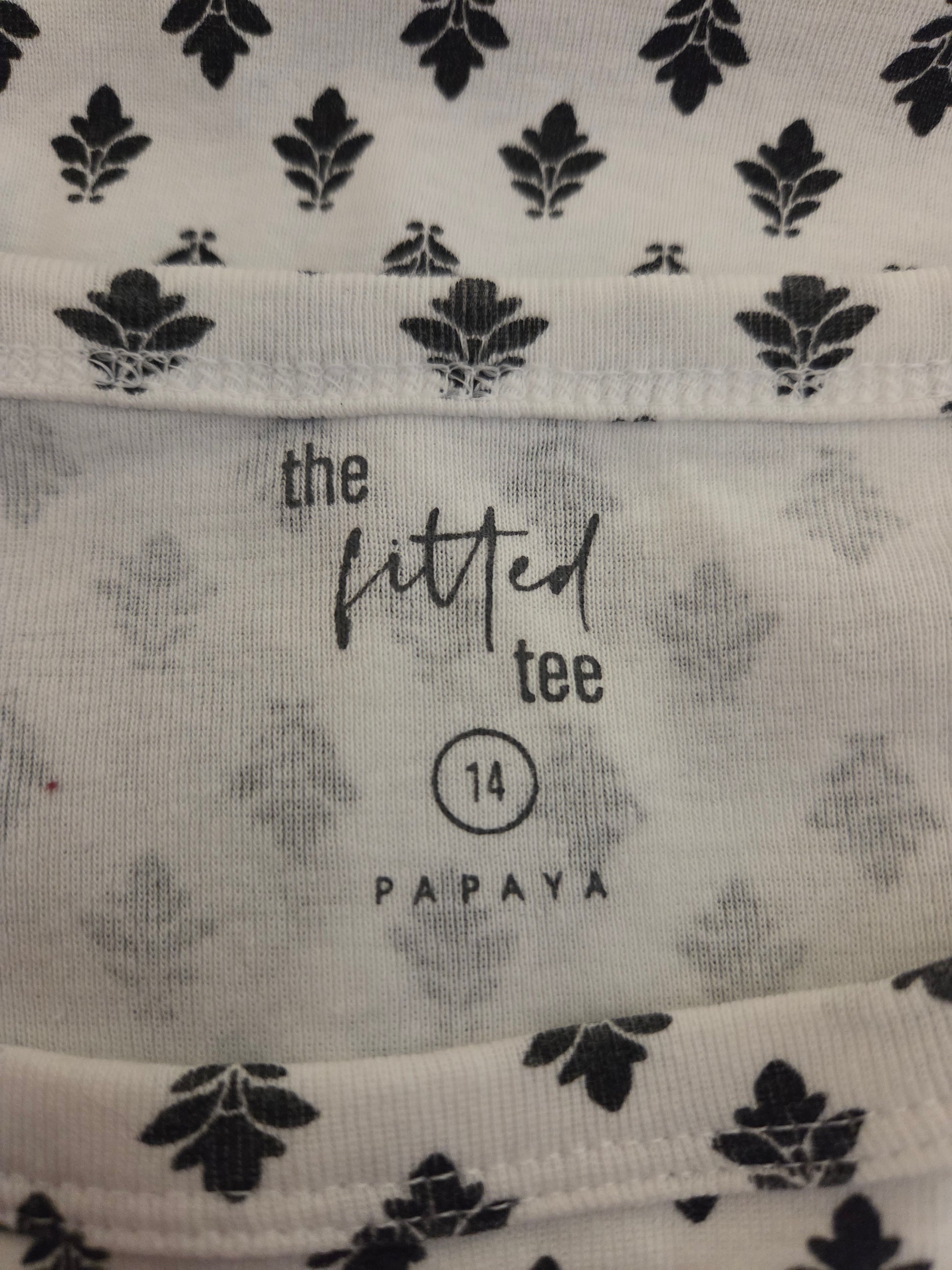 Close-up of fabric with black leaf pattern and 'the fitted tee' branding.