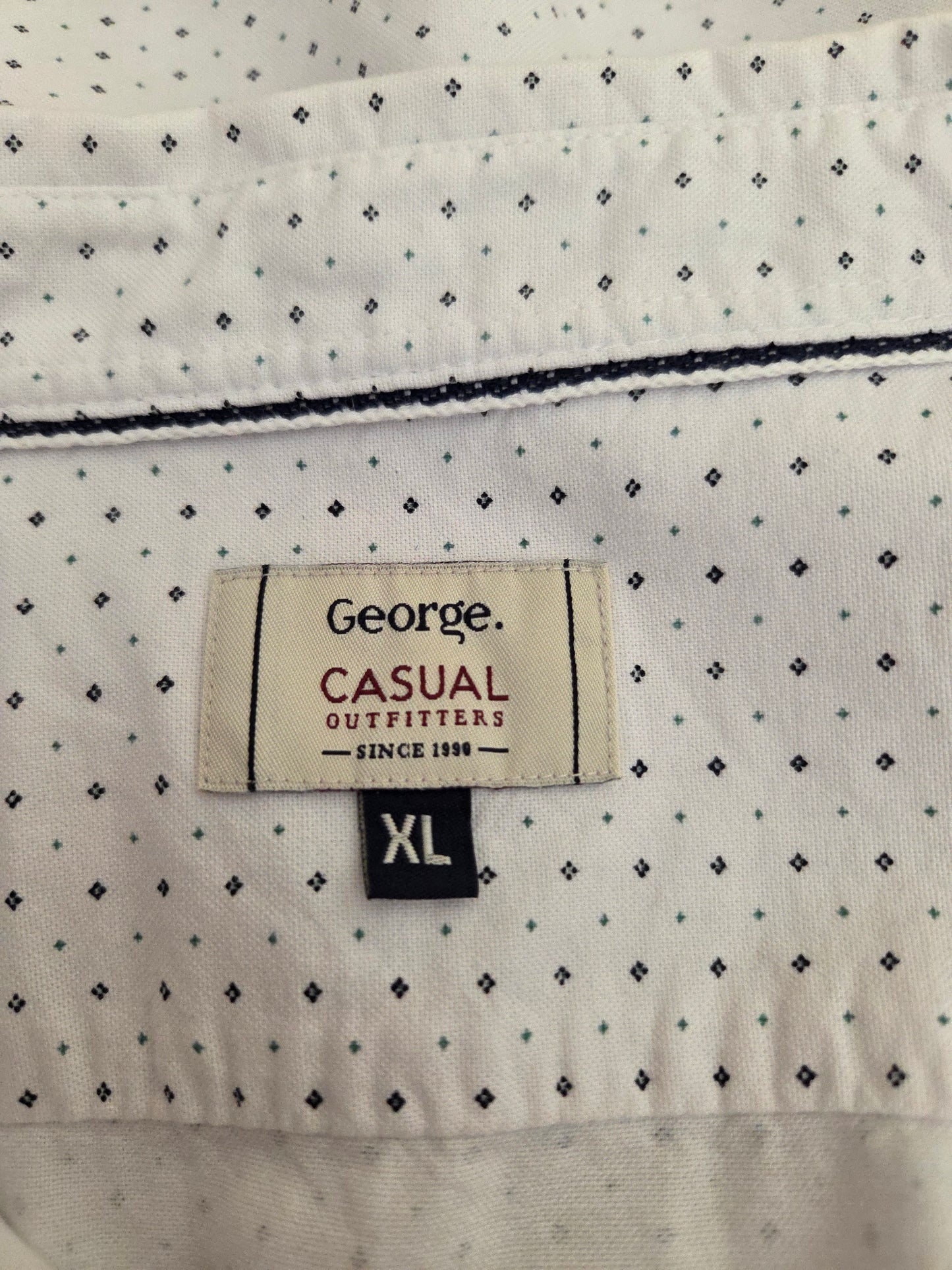Close-up of a shirt label with 'George Casual Outfitters' on a white shirt with black patterns.