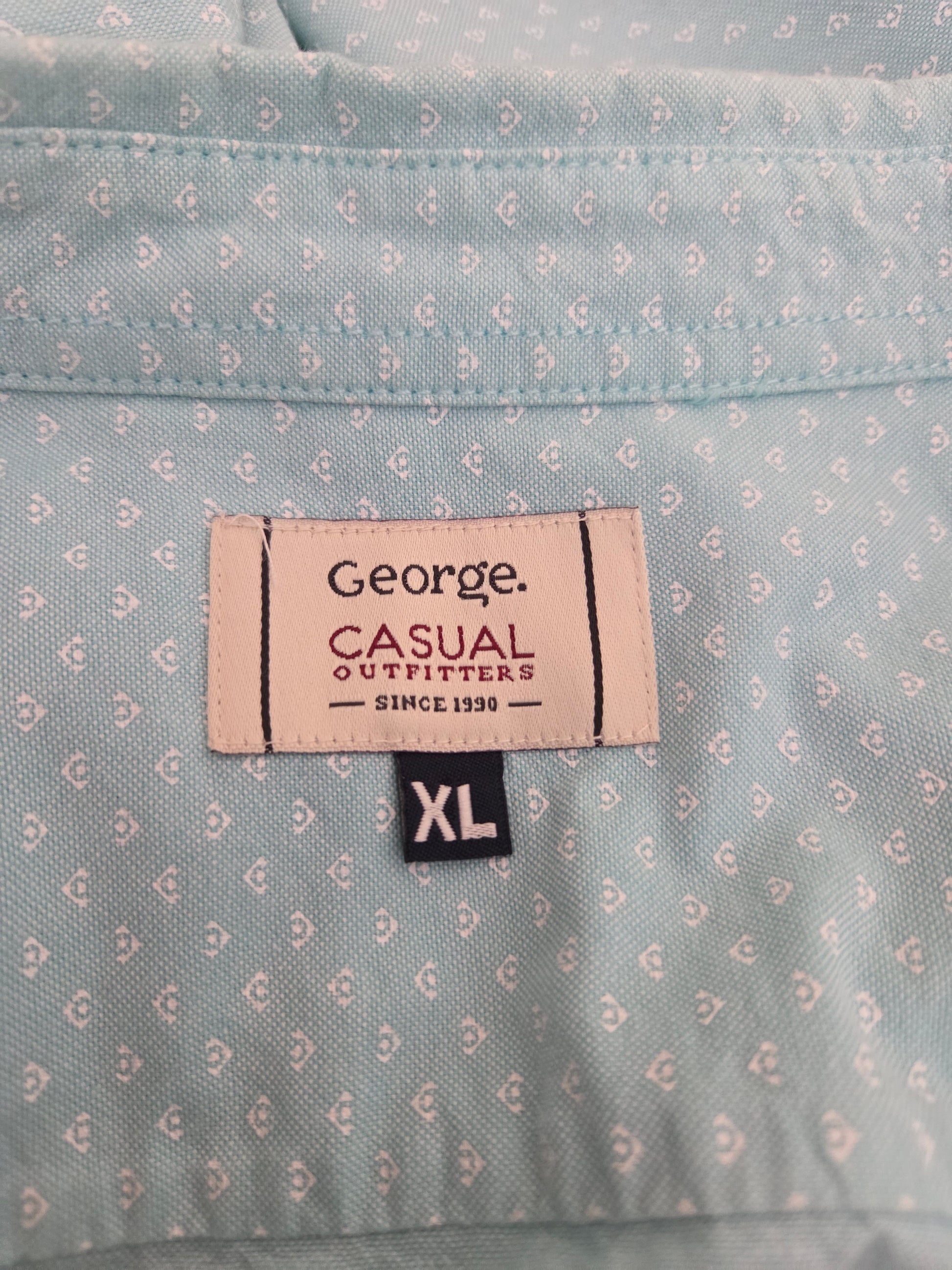 Close-up of a shirt label on a mint green patterned shirt with 'George Casual Outfitters' branding.