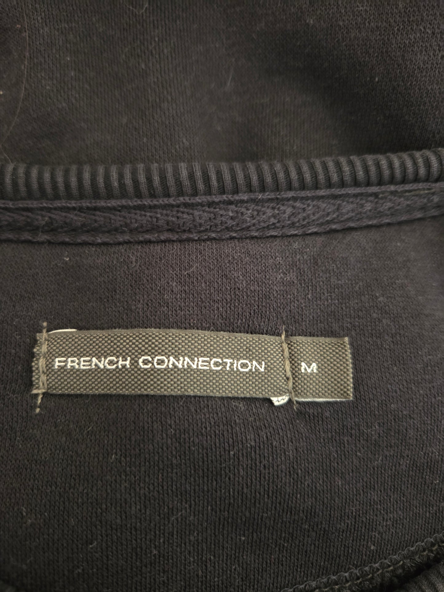 Close-up of a 'French Connection' label on a black garment with textured details.