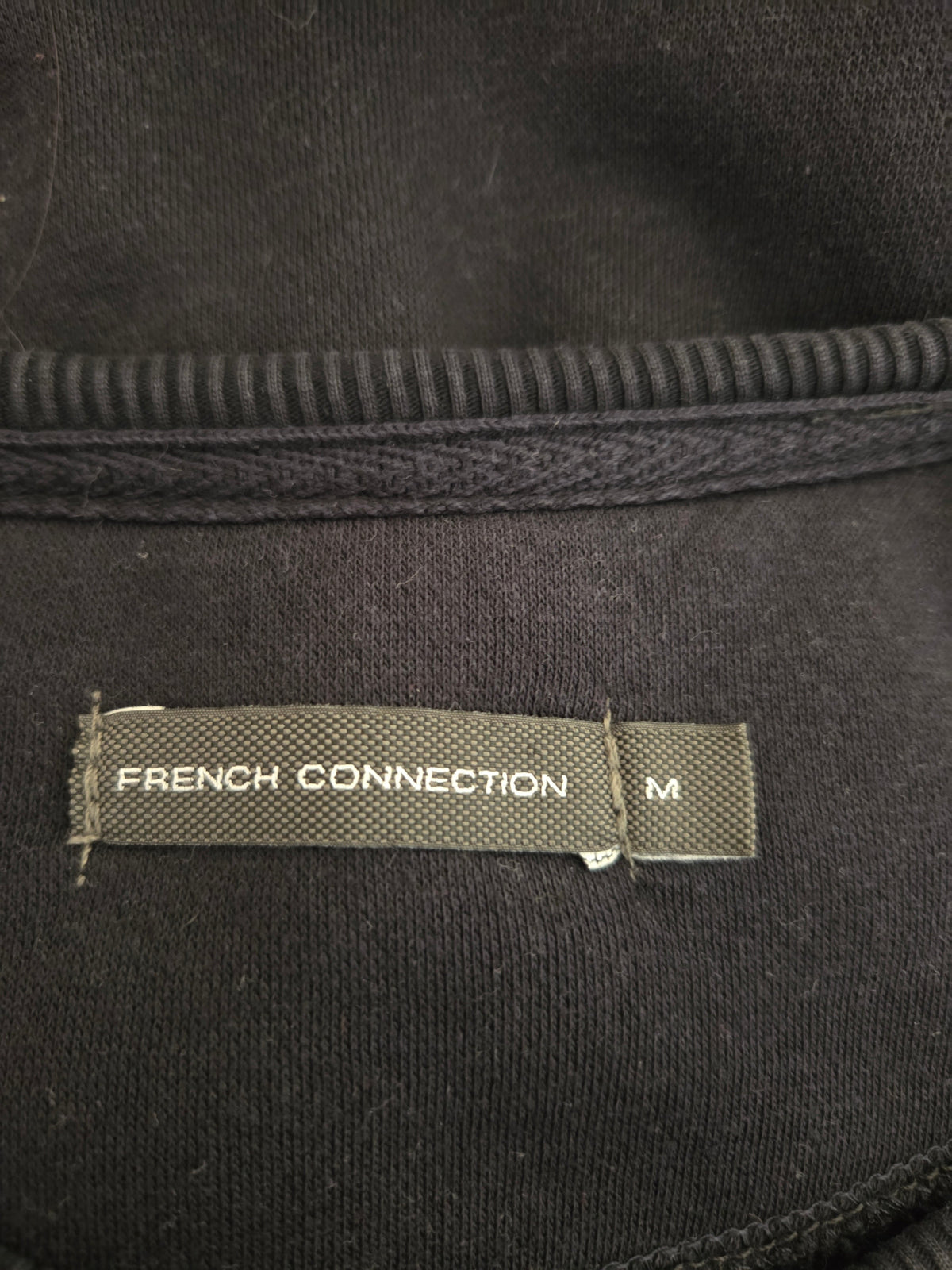 Close-up of a 'French Connection' label on a black garment with textured details.