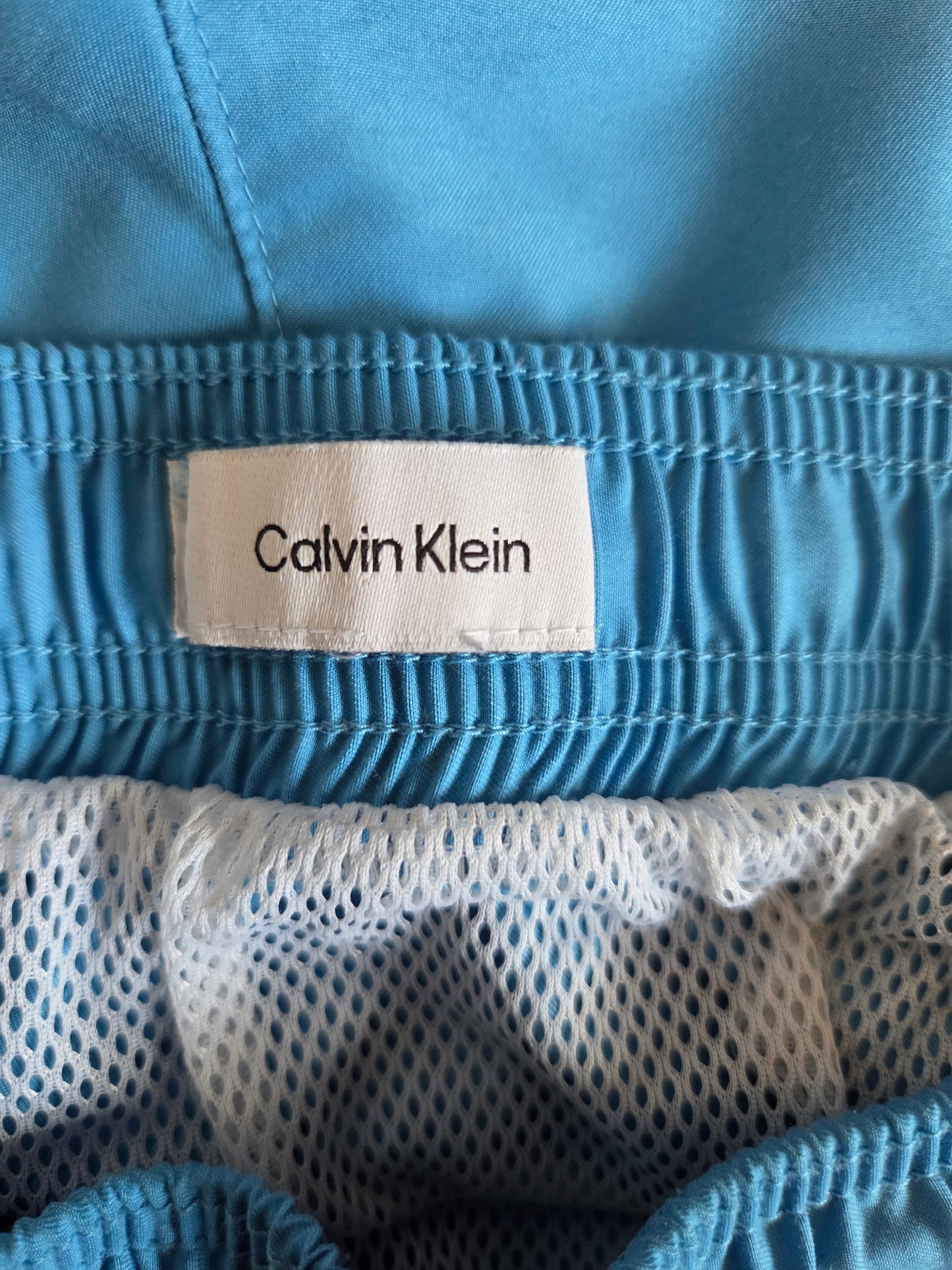 Close-up of a Calvin Klein label on a blue garment with mesh fabric.