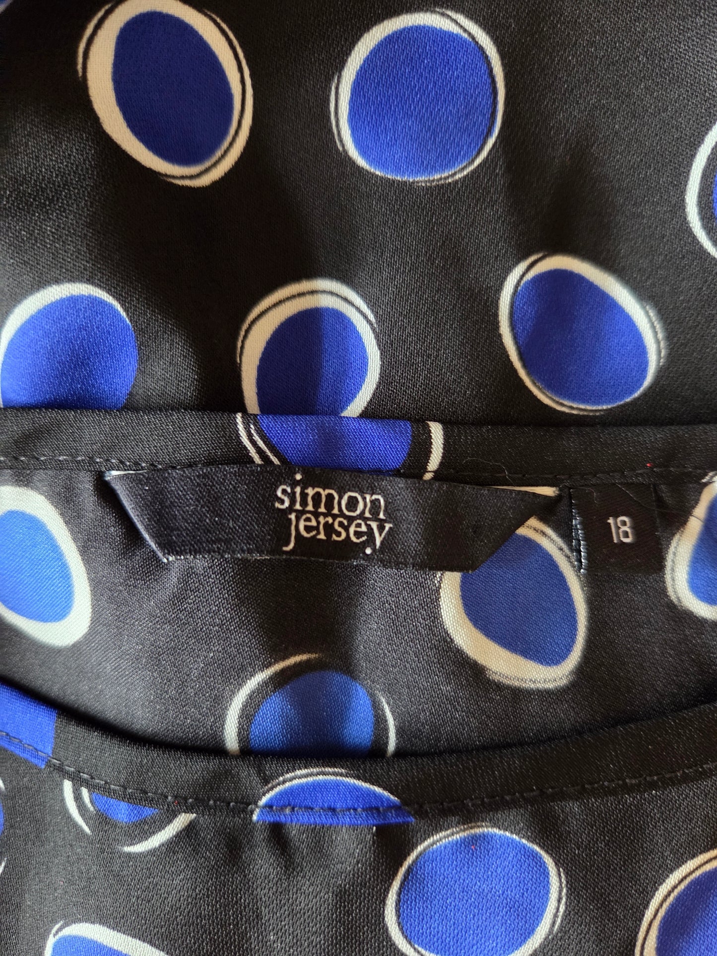 Black fabric with blue and white polka dots and 'Simon Jersey' label.
