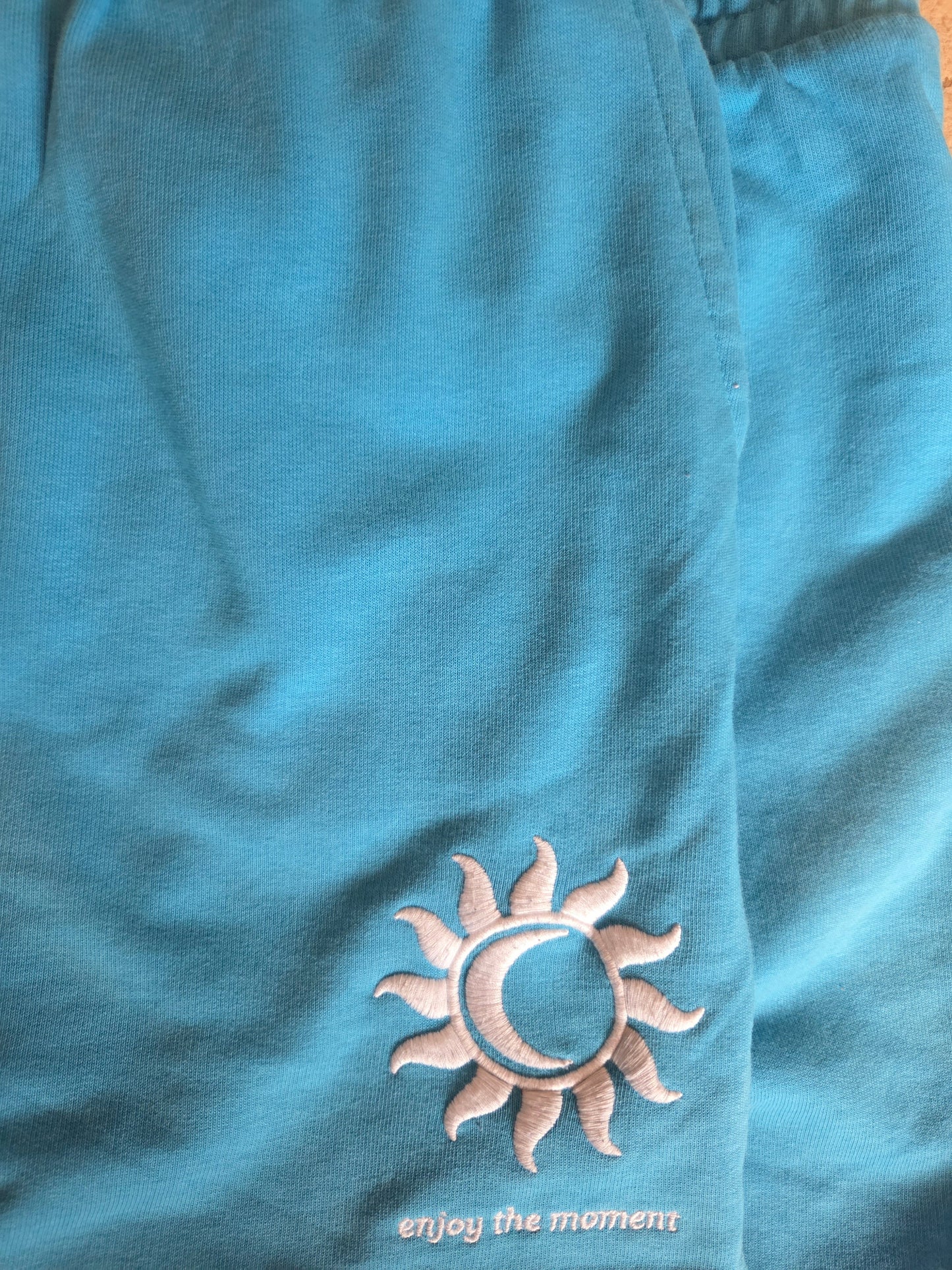 Blue shorts with a sun and moon emblem and 'enjoy the moment' text.