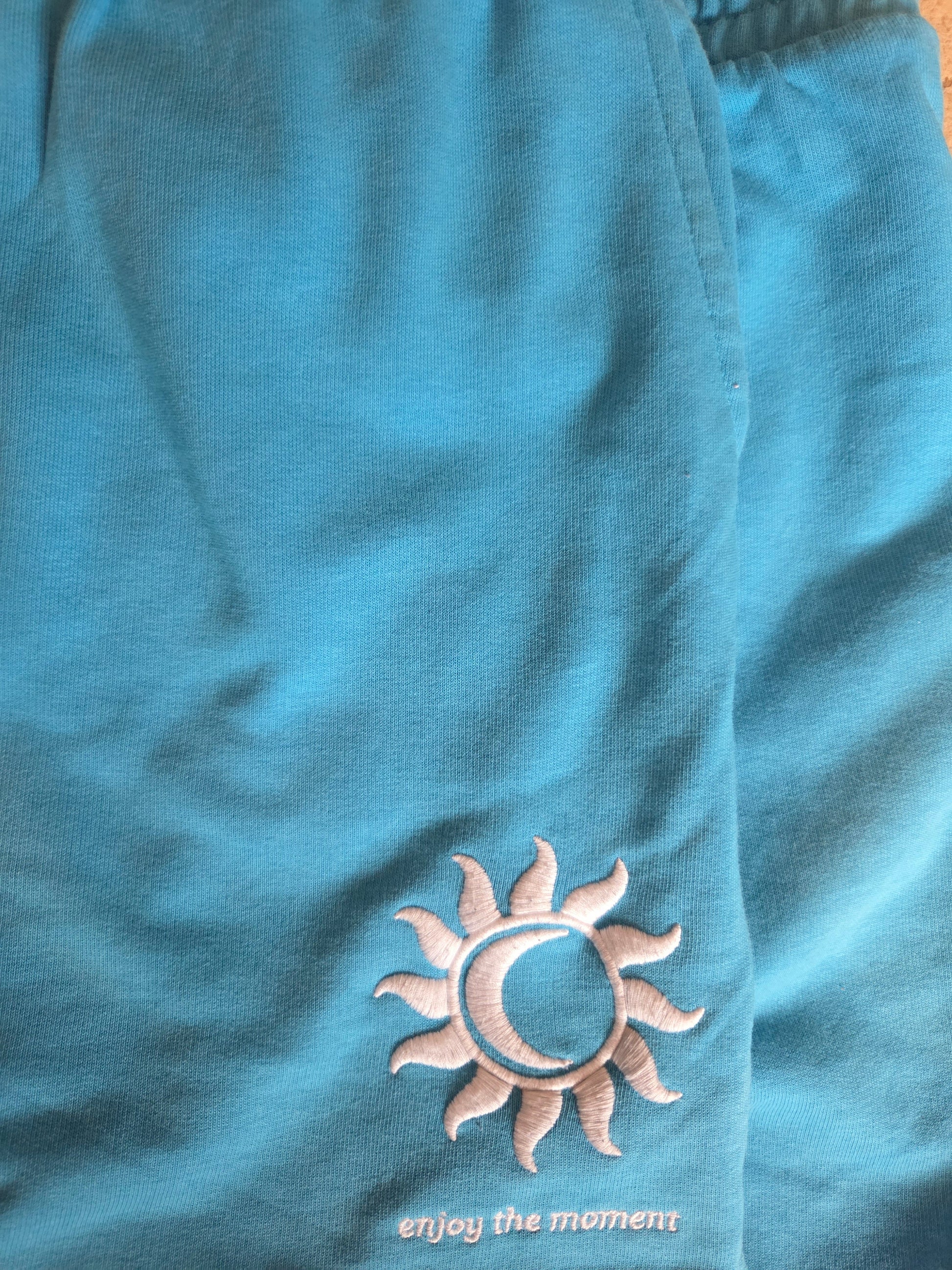 Blue shorts with a sun and moon emblem and 'enjoy the moment' text.