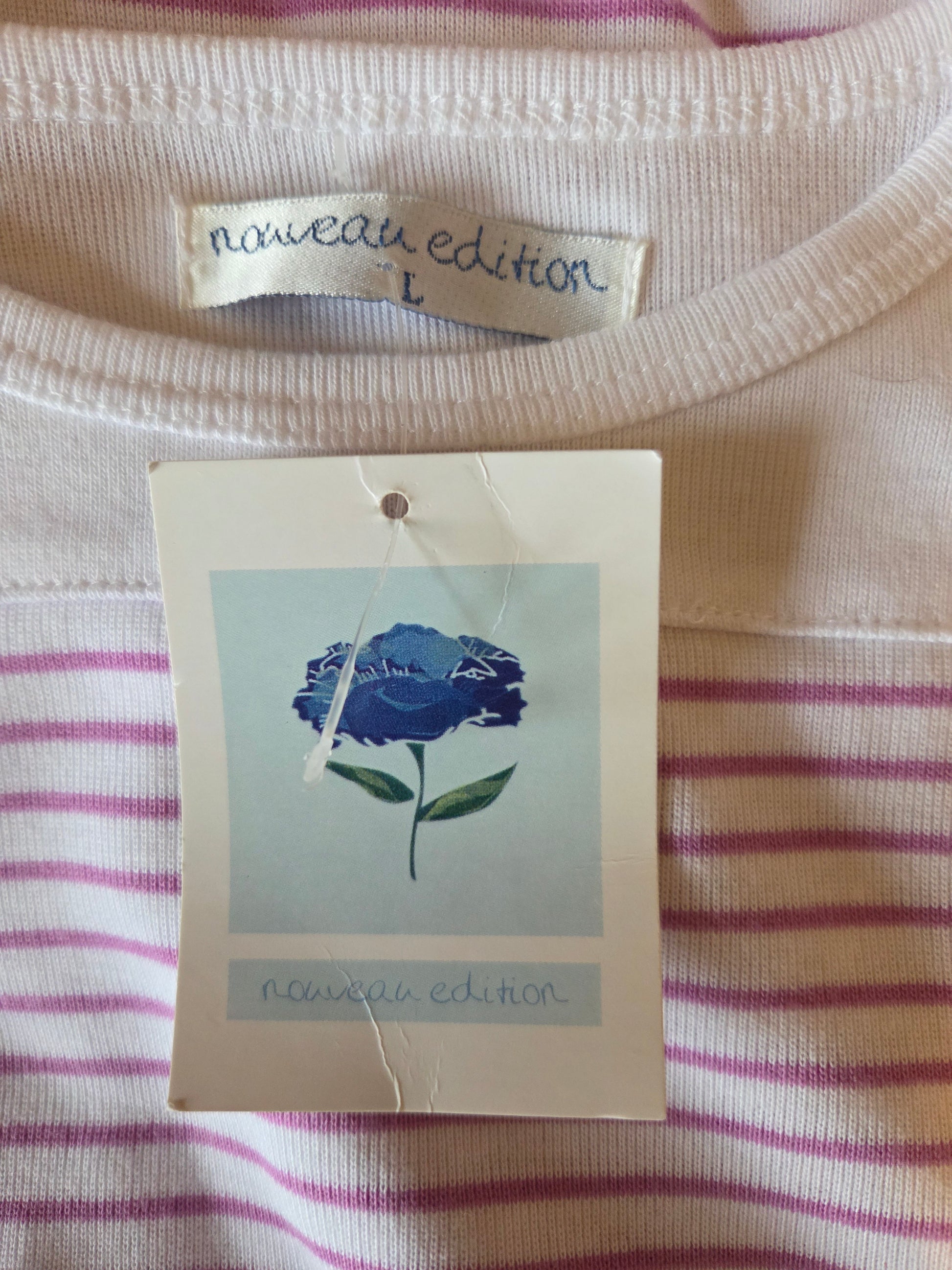 Close-up of a striped shirt with a blue rose tag and 'nouveau edition' label.