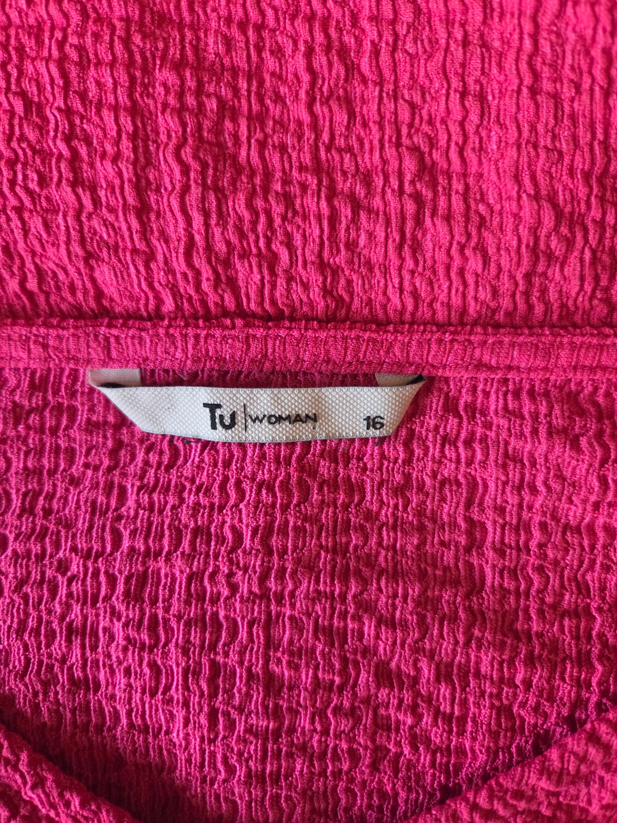 Close-up of a pink textured fabric with a TU Woman size label on a pink background