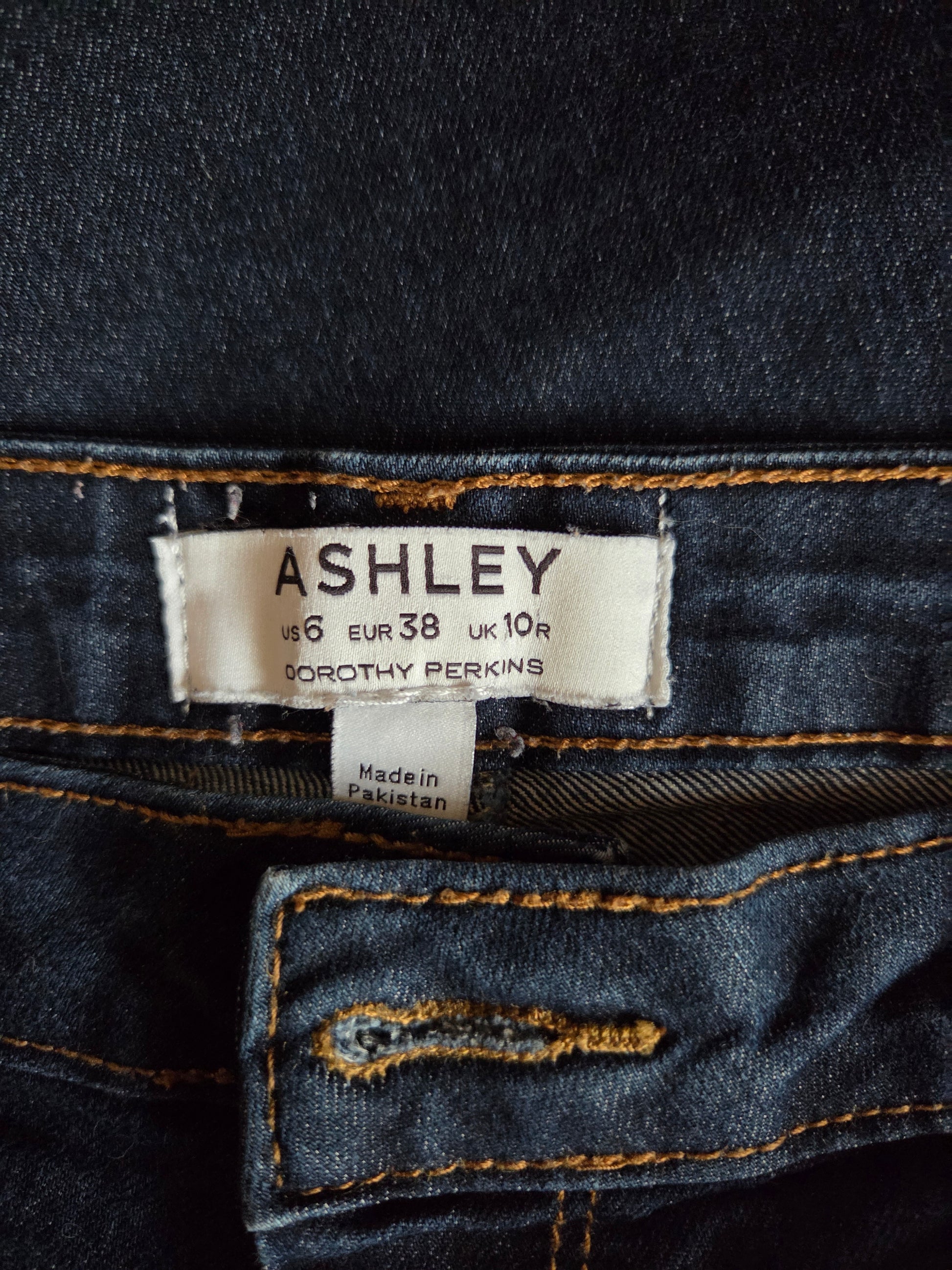 Close-up of a denim label with 'Ashley' and 'Dorothy Perkins' text on a dark blue fabric background.