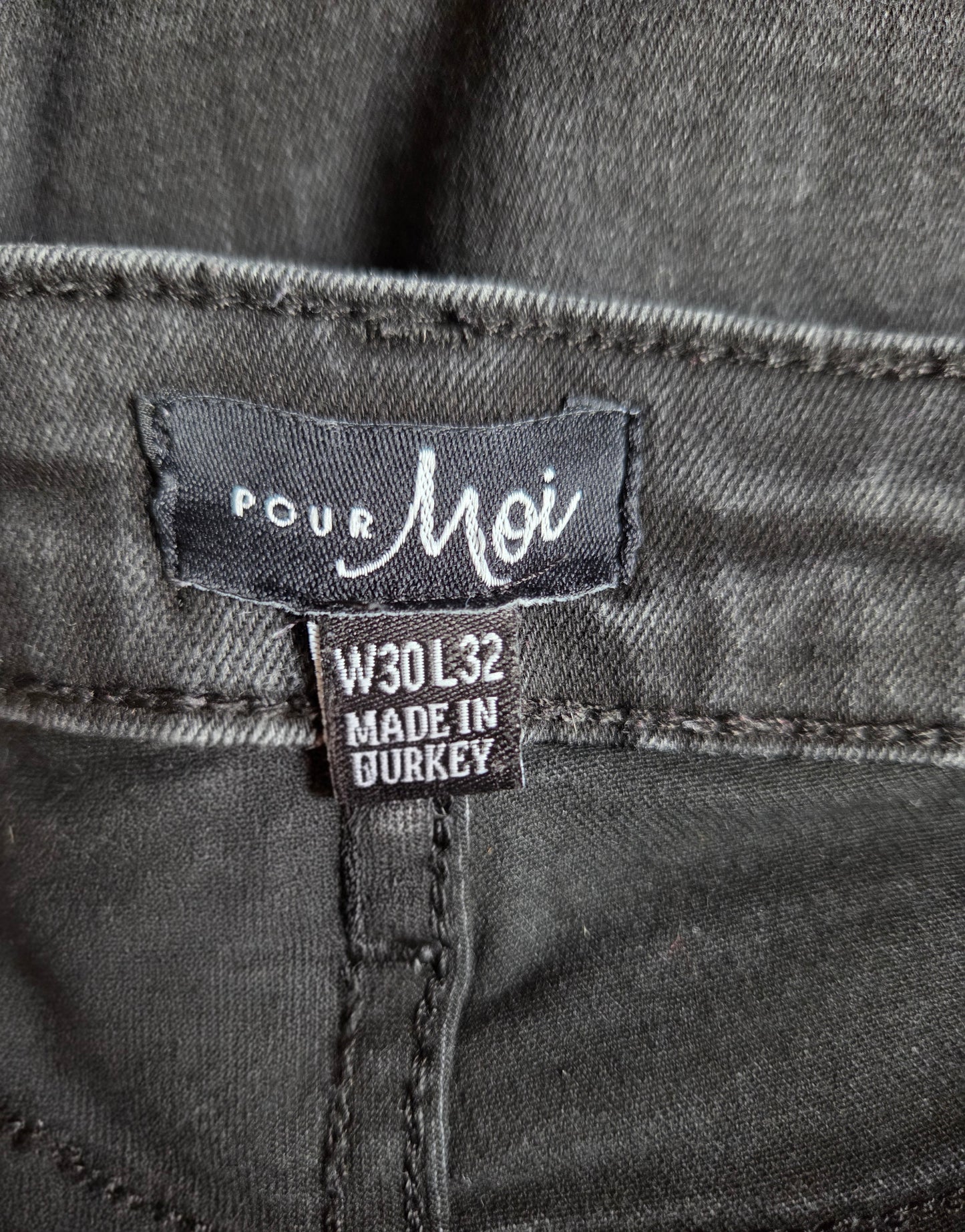 Close-up of a denim label on a gray denim fabric with 'Pour Moi' branding.