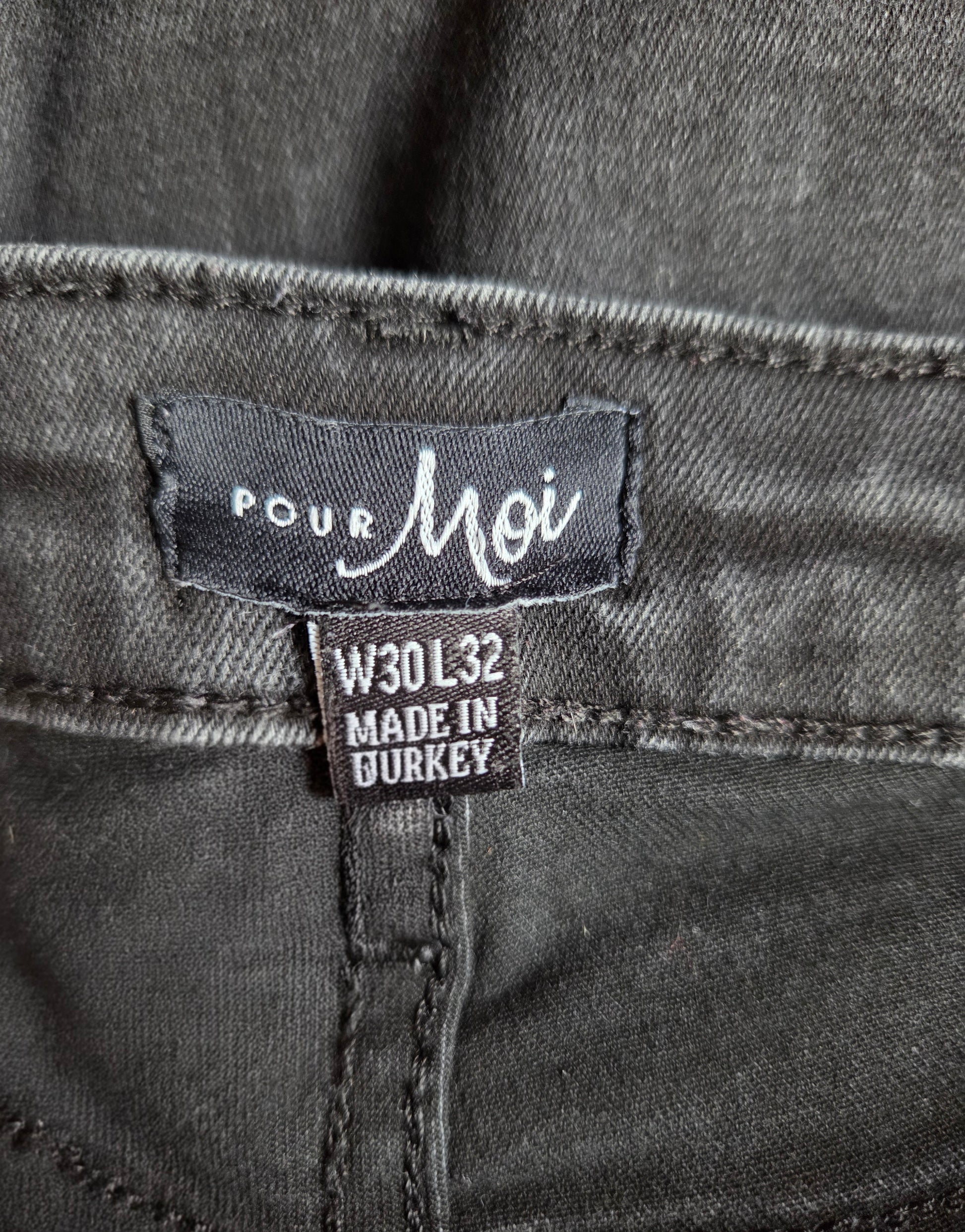 Close-up of a denim label on a gray denim fabric with 'Pour Moi' branding.