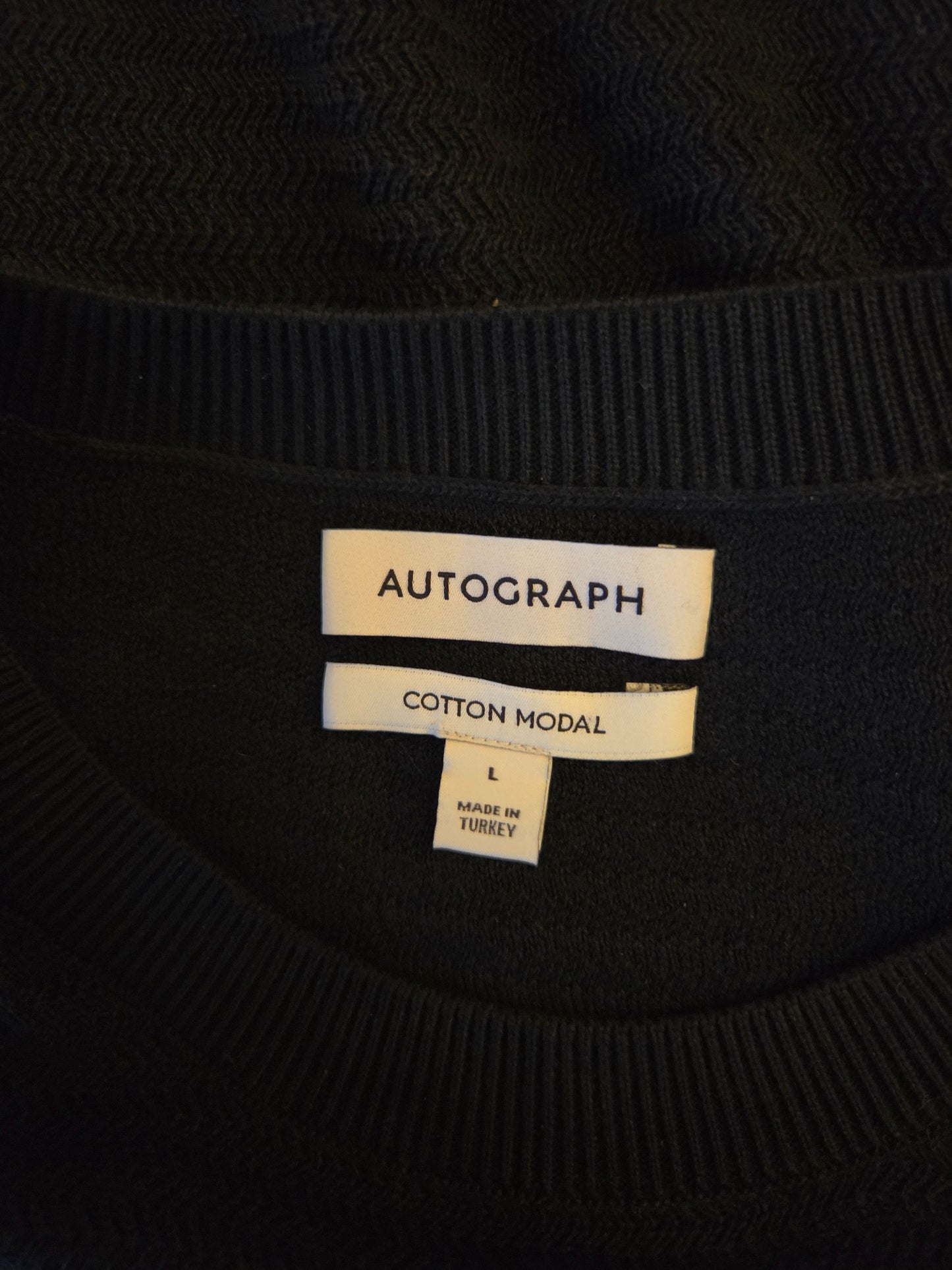 Black sweater with 'Autograph' label on a dark background