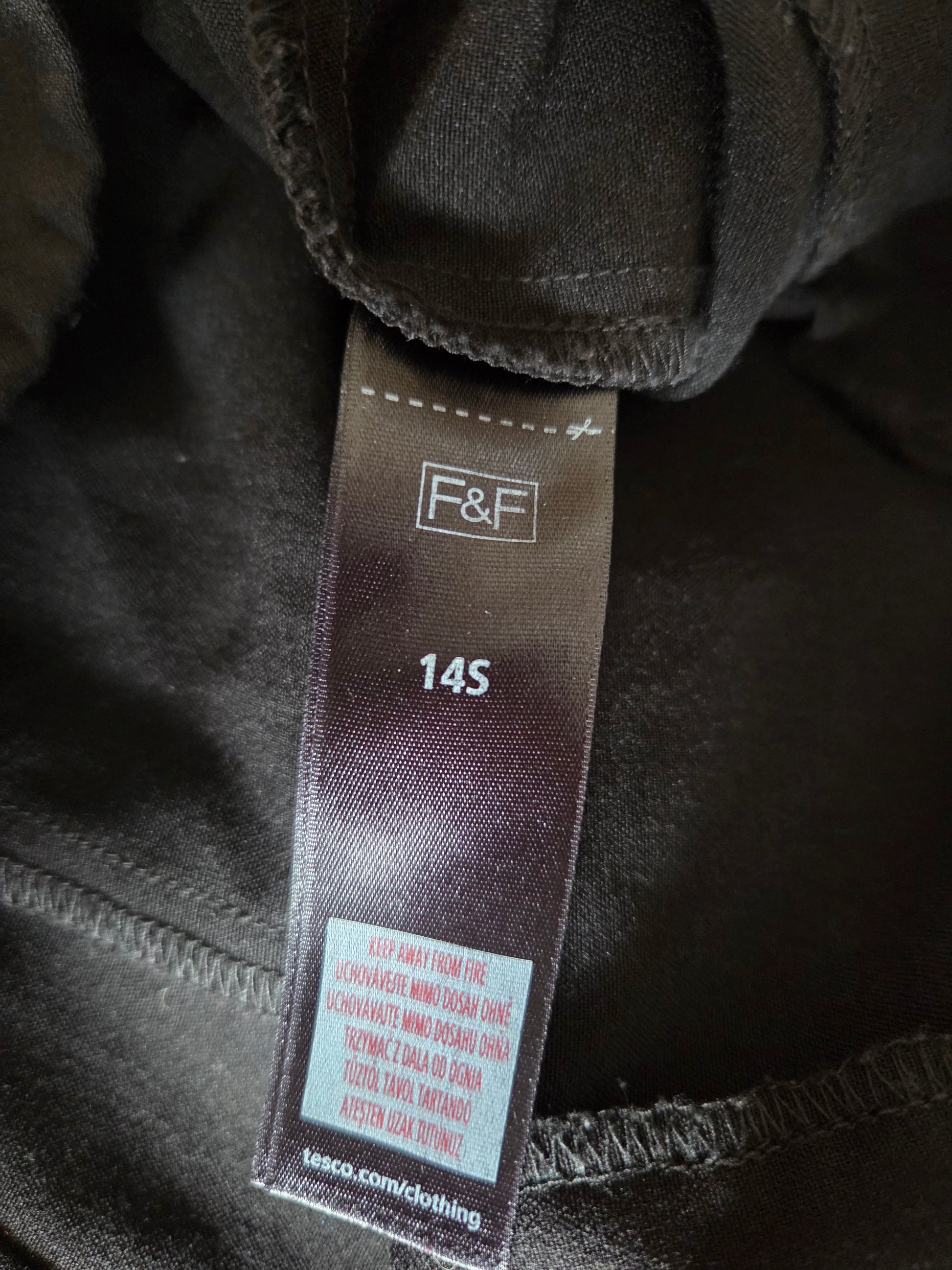 Clothing tag with 'F&F' brand on a dark fabric background