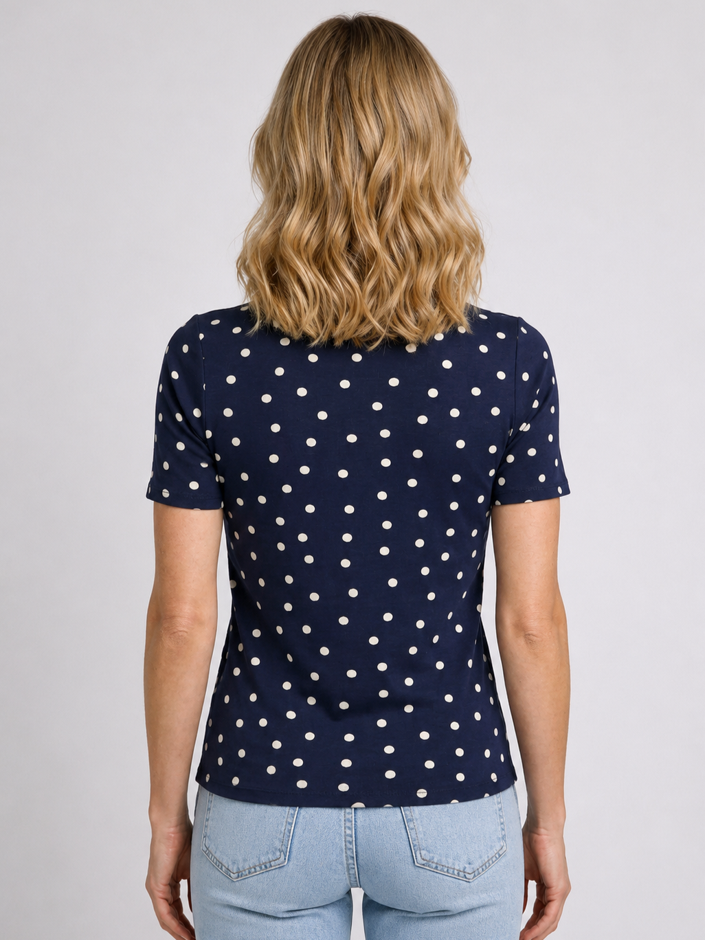 Woman wearing a navy blue polka dot top with light blue jeans