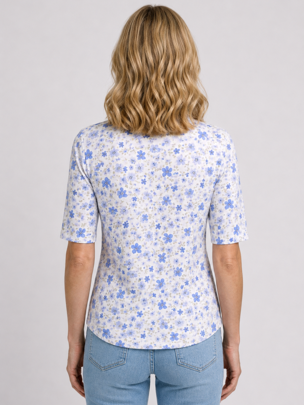 Woman wearing a white top with blue floral pattern and blue jeans 