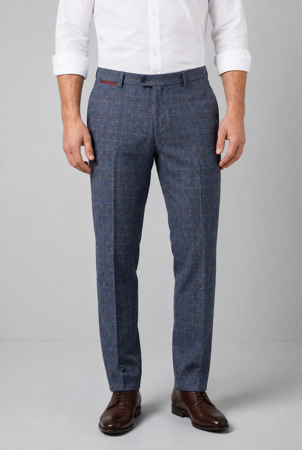A man wearing blue windowpane plaid trousers, a white long-sleeve dress shirt, and brown leather dress shoes