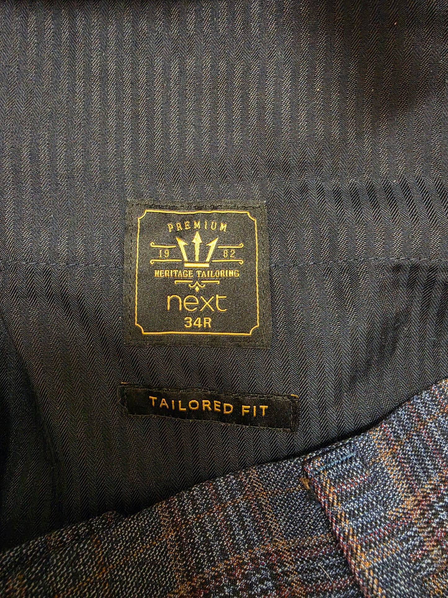 Close-up of a gold 'next' brand label and a black 'TAILORED FIT' tag.