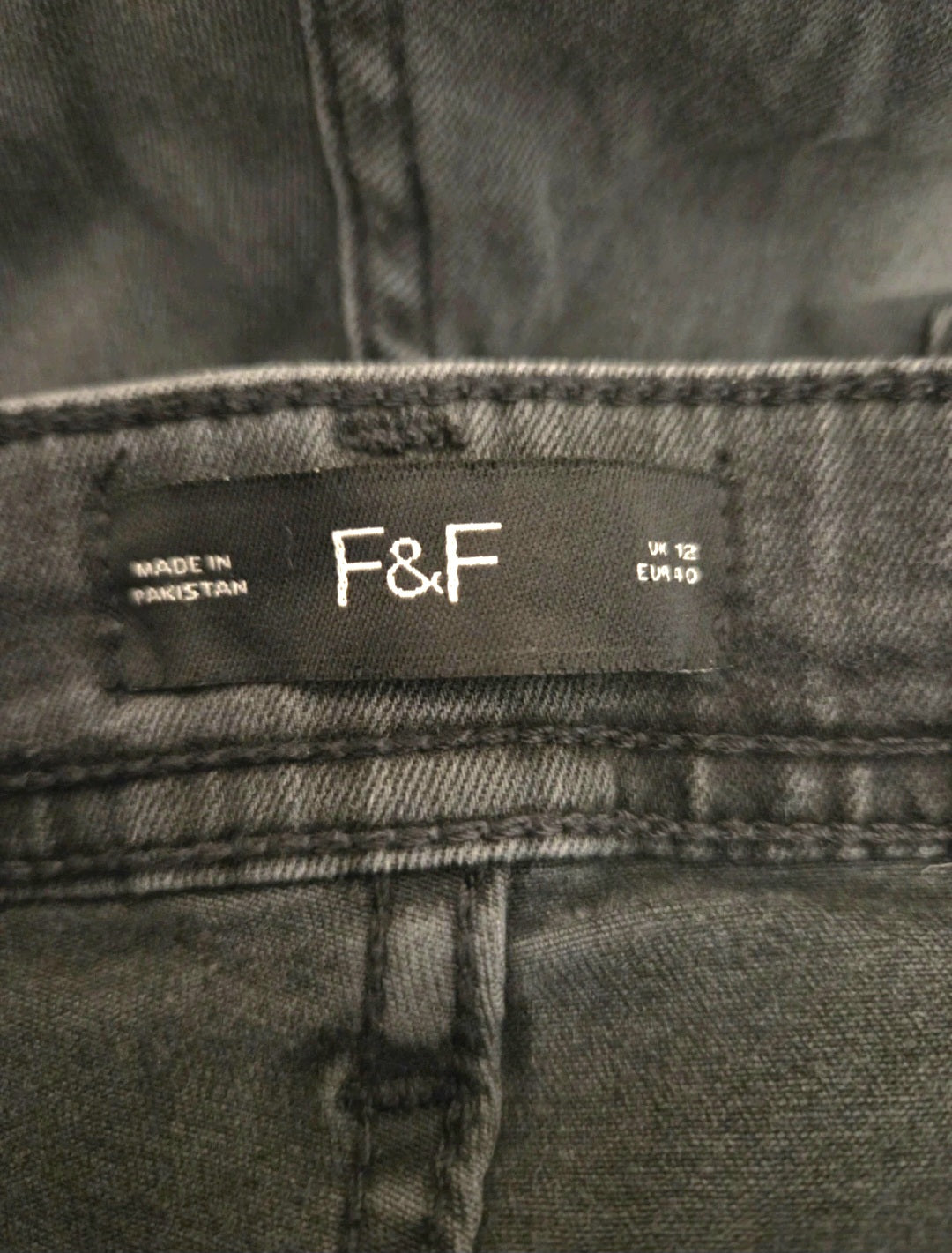 Close-up of a black label with 'F&F' branding on gray denim fabric.
