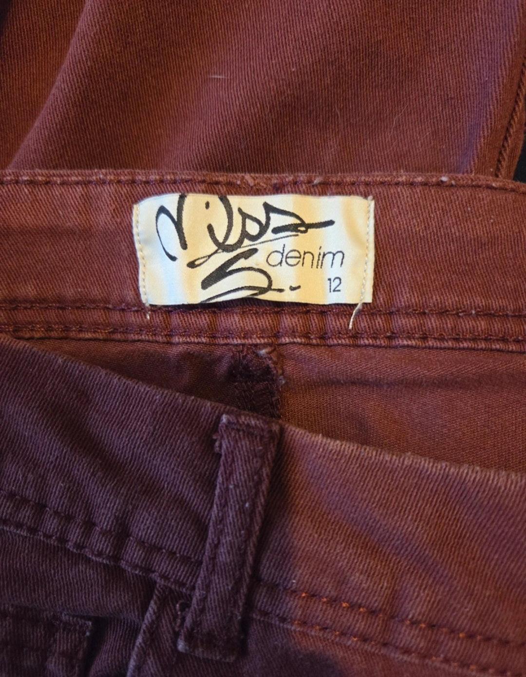 Close-up of a size label on a piece of burgundy denim fabric.