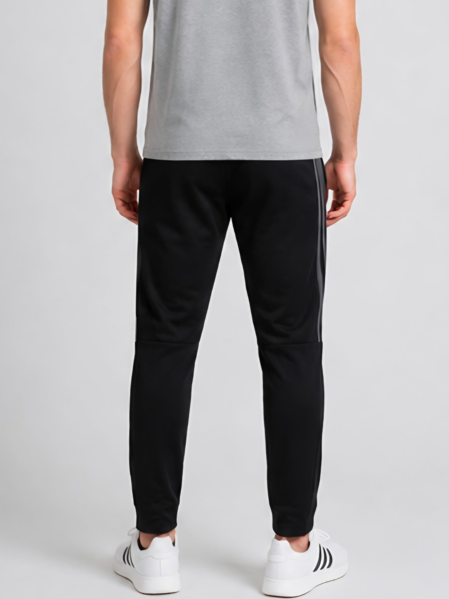 Man wearing black Adidas tracksuit bottoms with grey stripes back view