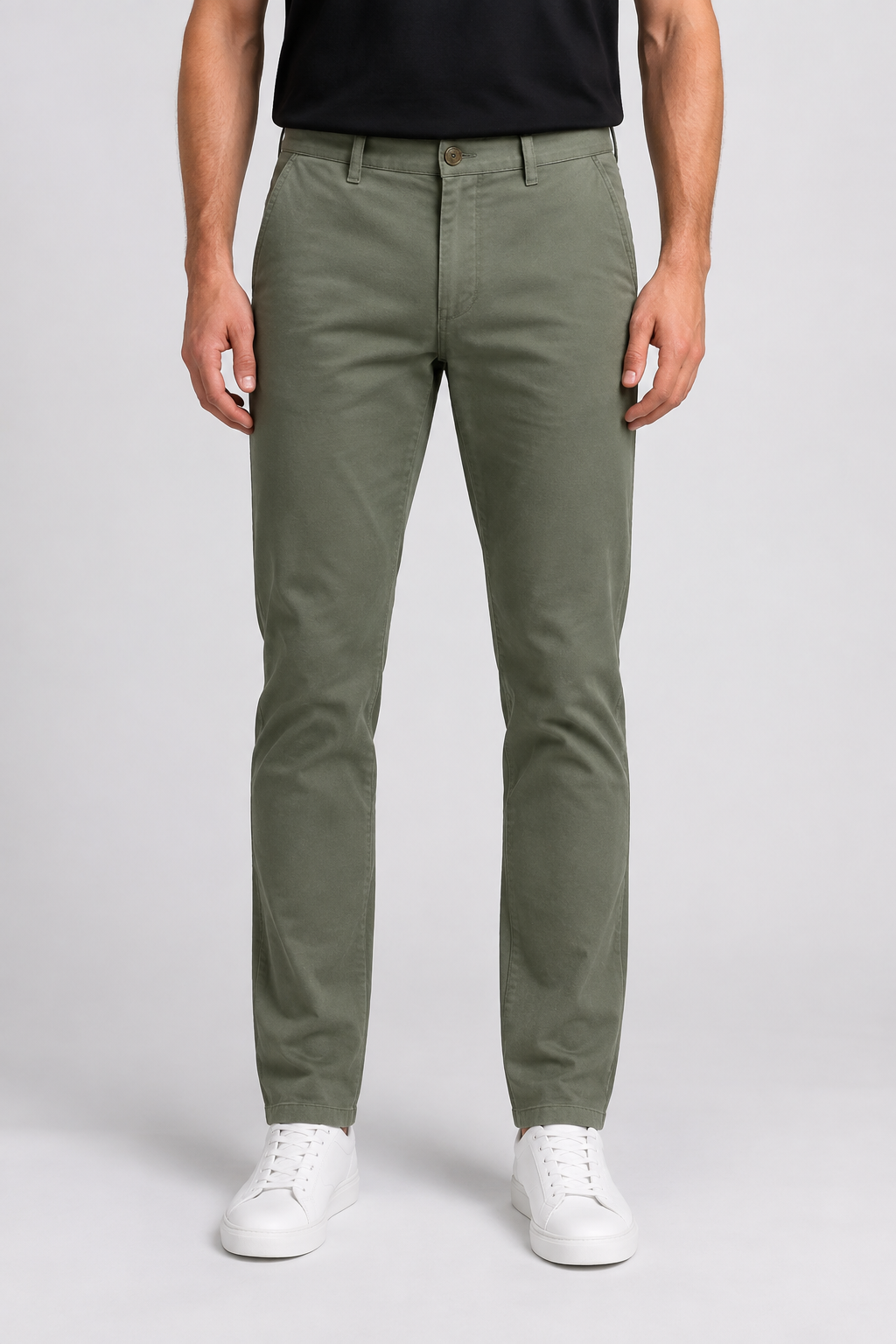 A man wearing slim-fit olive green chinos, a black t-shirt, and white trainers.